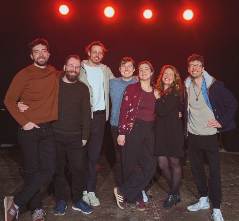Sept comédiens serrés les uns contre les autres sur scène, tout sourire
